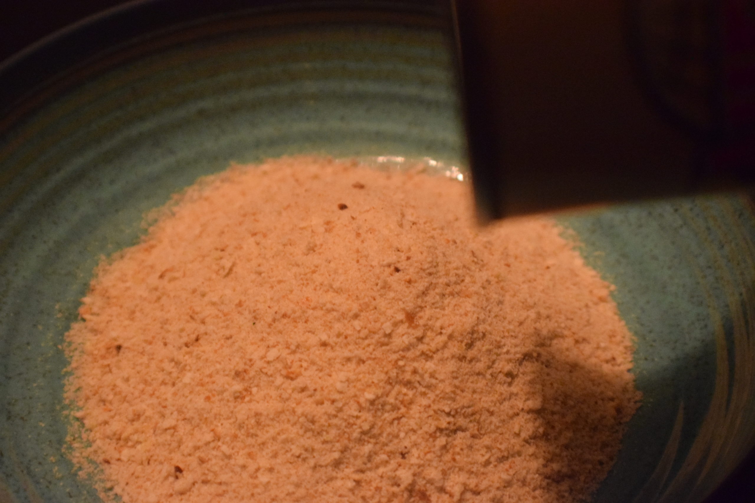 pouring bread crumbs into a blue bowl