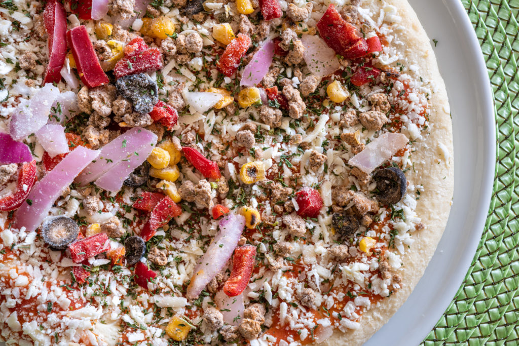 uncooked frozen pizza topped with peppers, onions, and corn