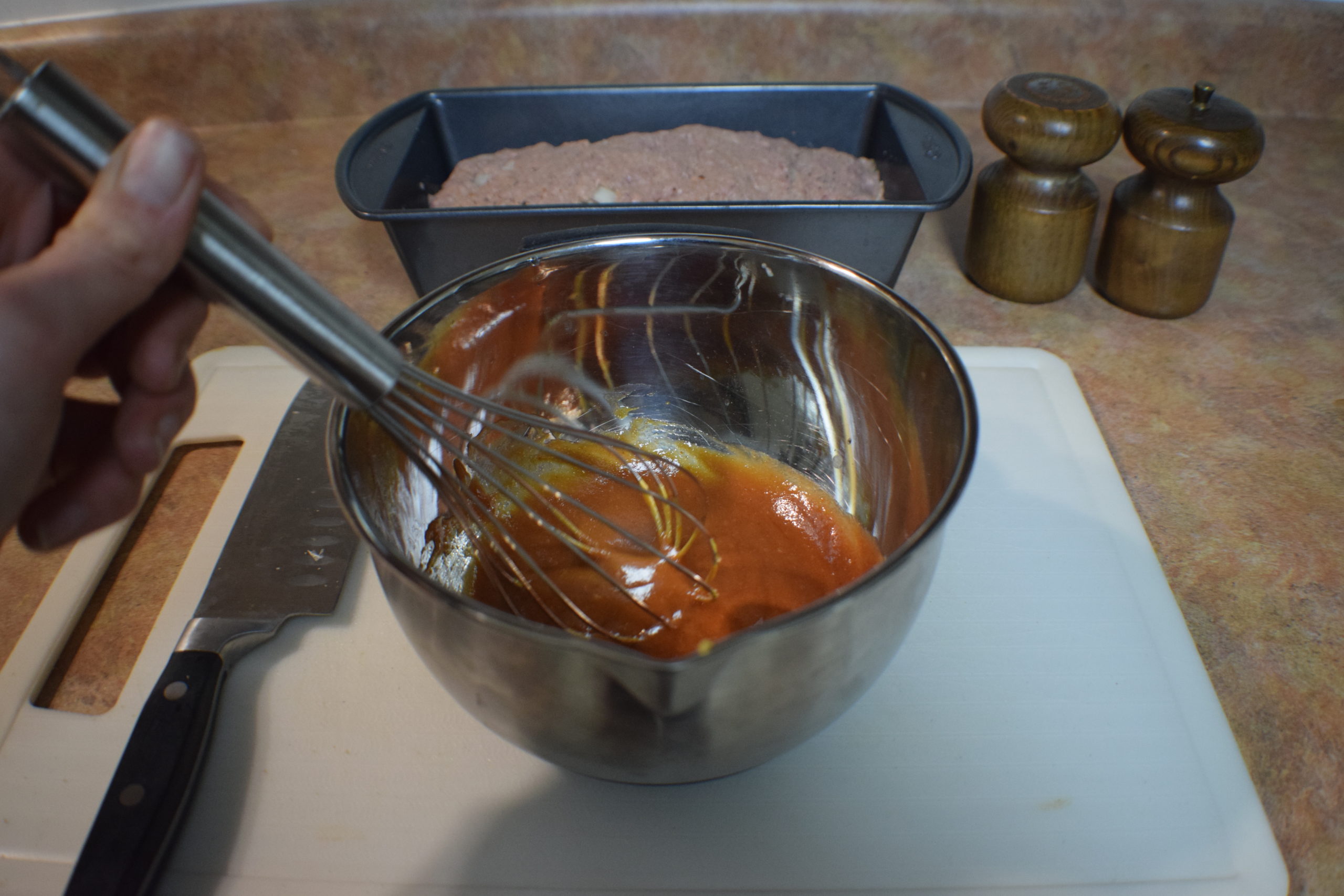 hand whisking red and yellow ingredients on white cutting board