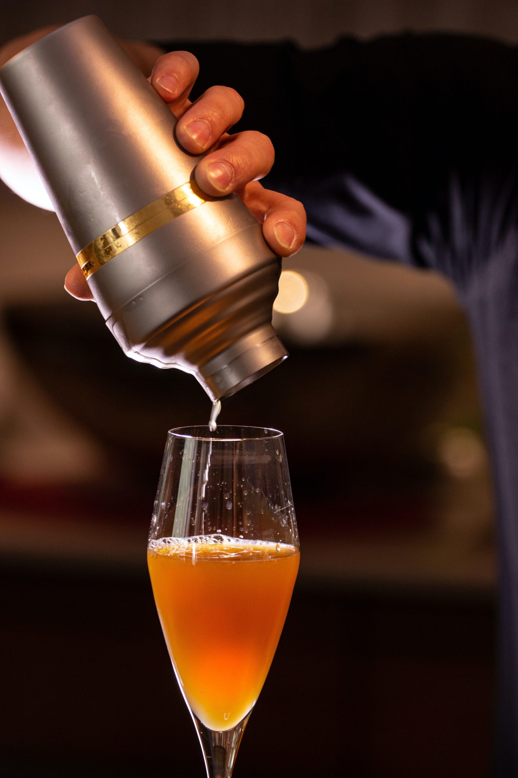 man pouring shaker into glass in dark lit room