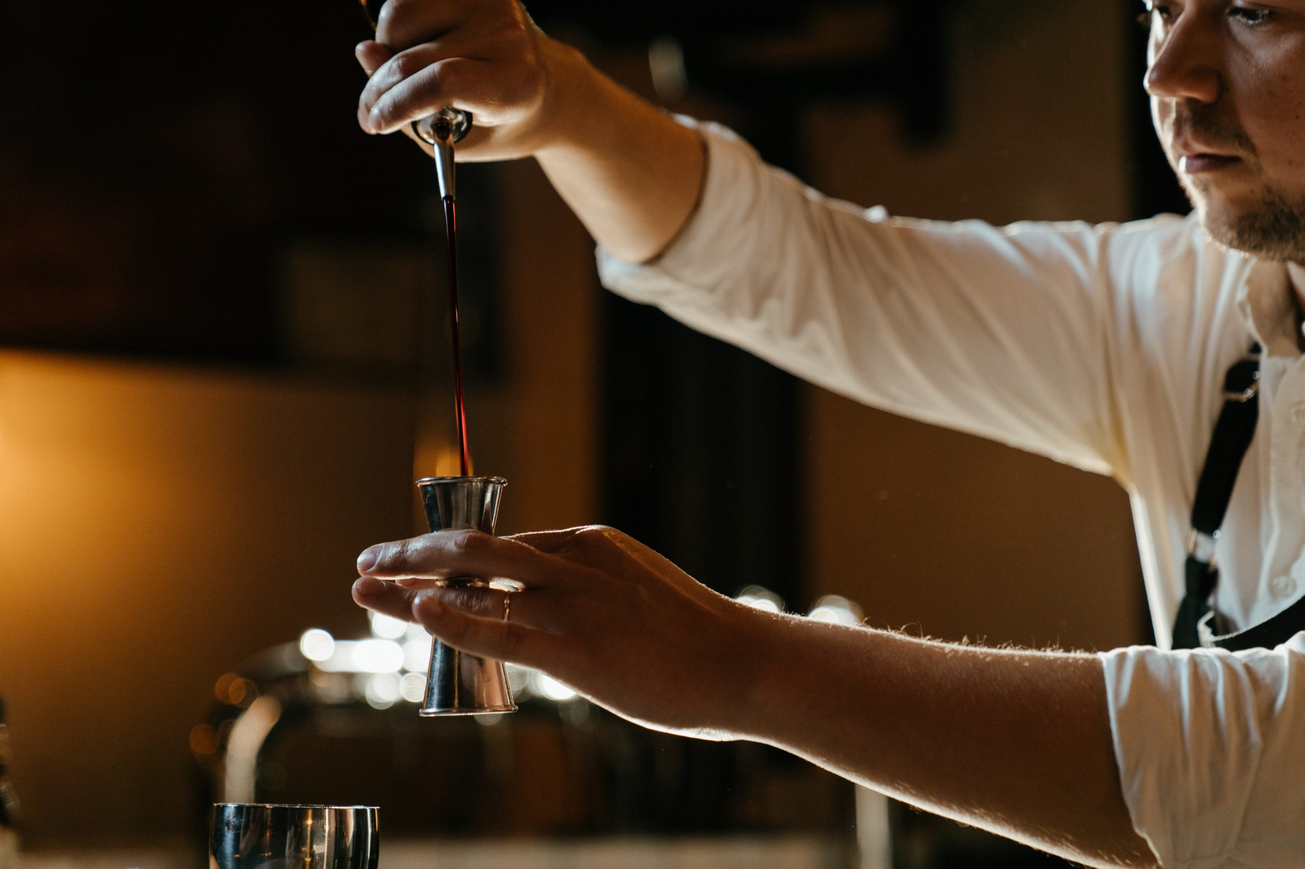 bartender pouring alcohol into a jigger in a bar