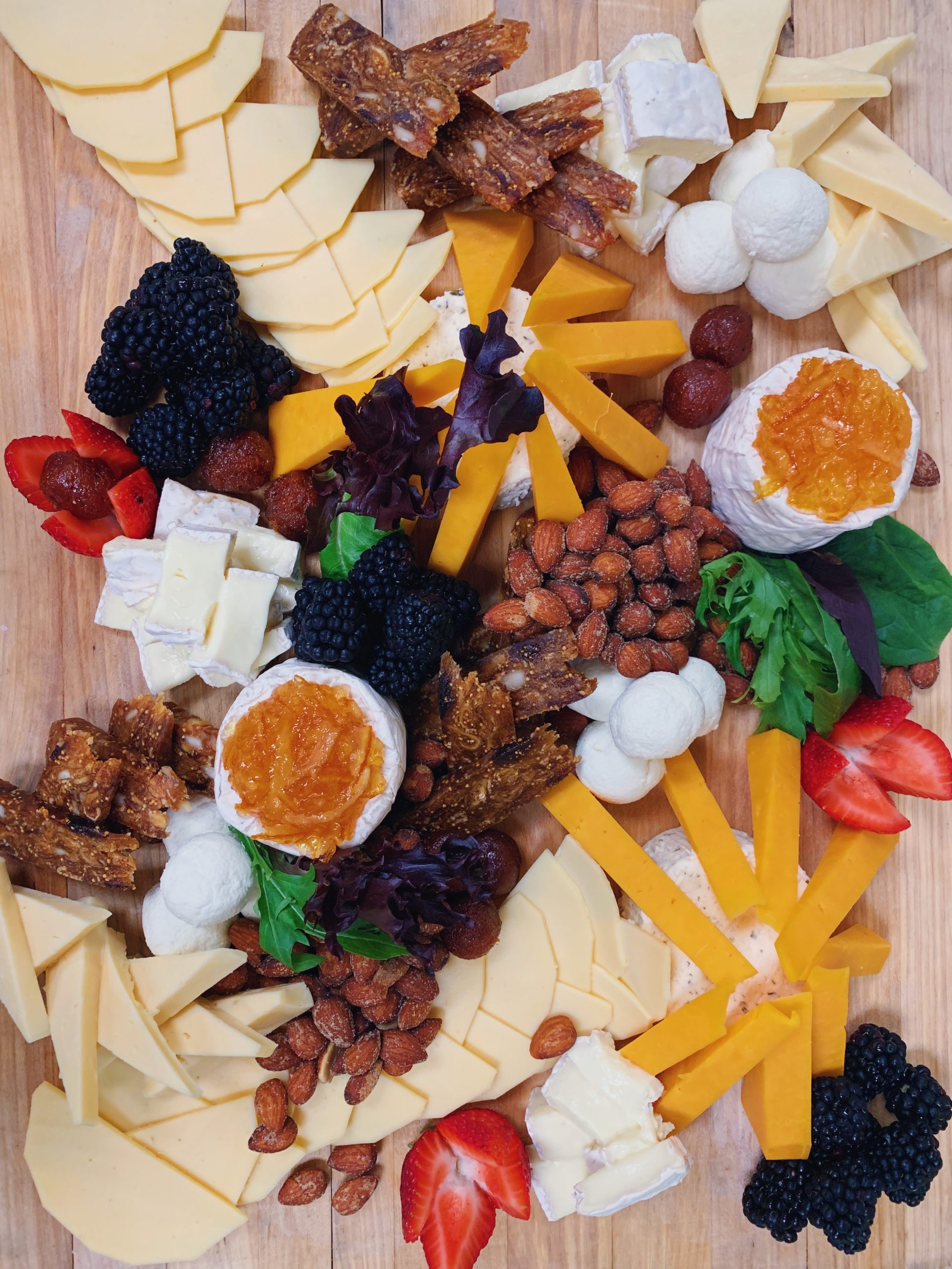 loaded and colorful platter of cheese, meat, fruit, candy peanuts and greens on a wood board