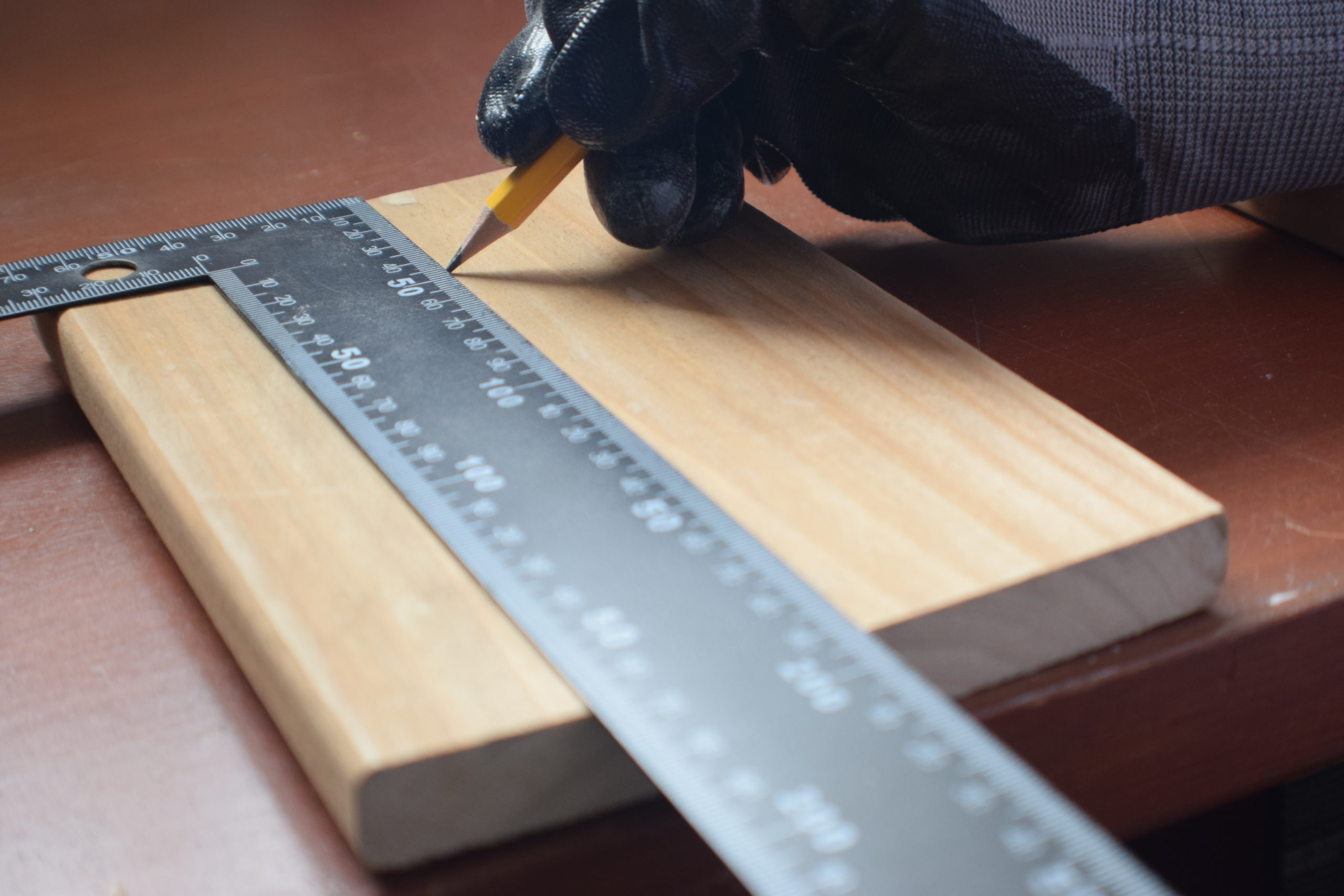 gloved hand penciling a straight line across wood