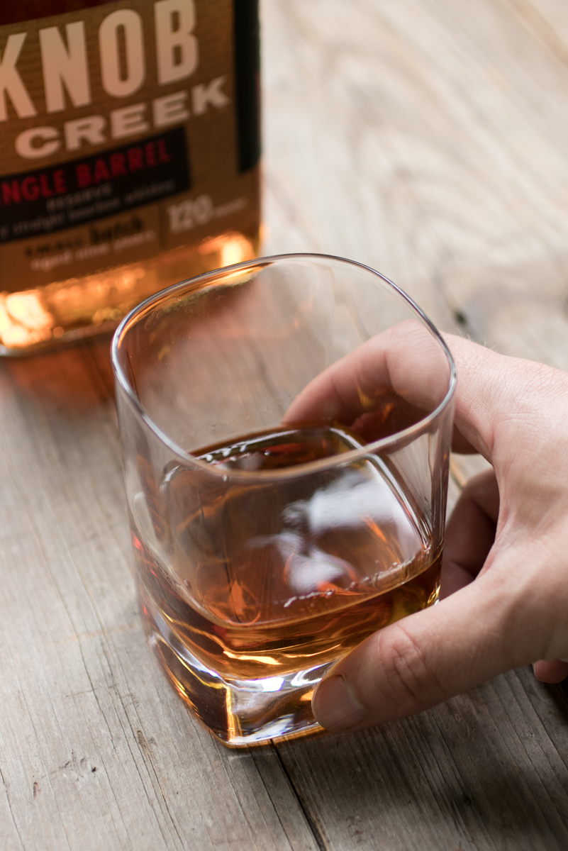 A whiskey rock glass accompanying a bottle of knob creek whiskey.