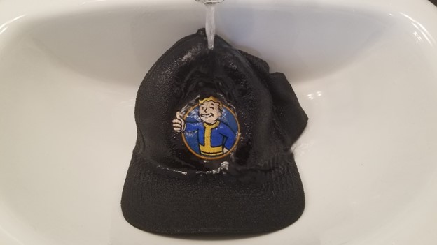 black baseball cap in a sink with water running