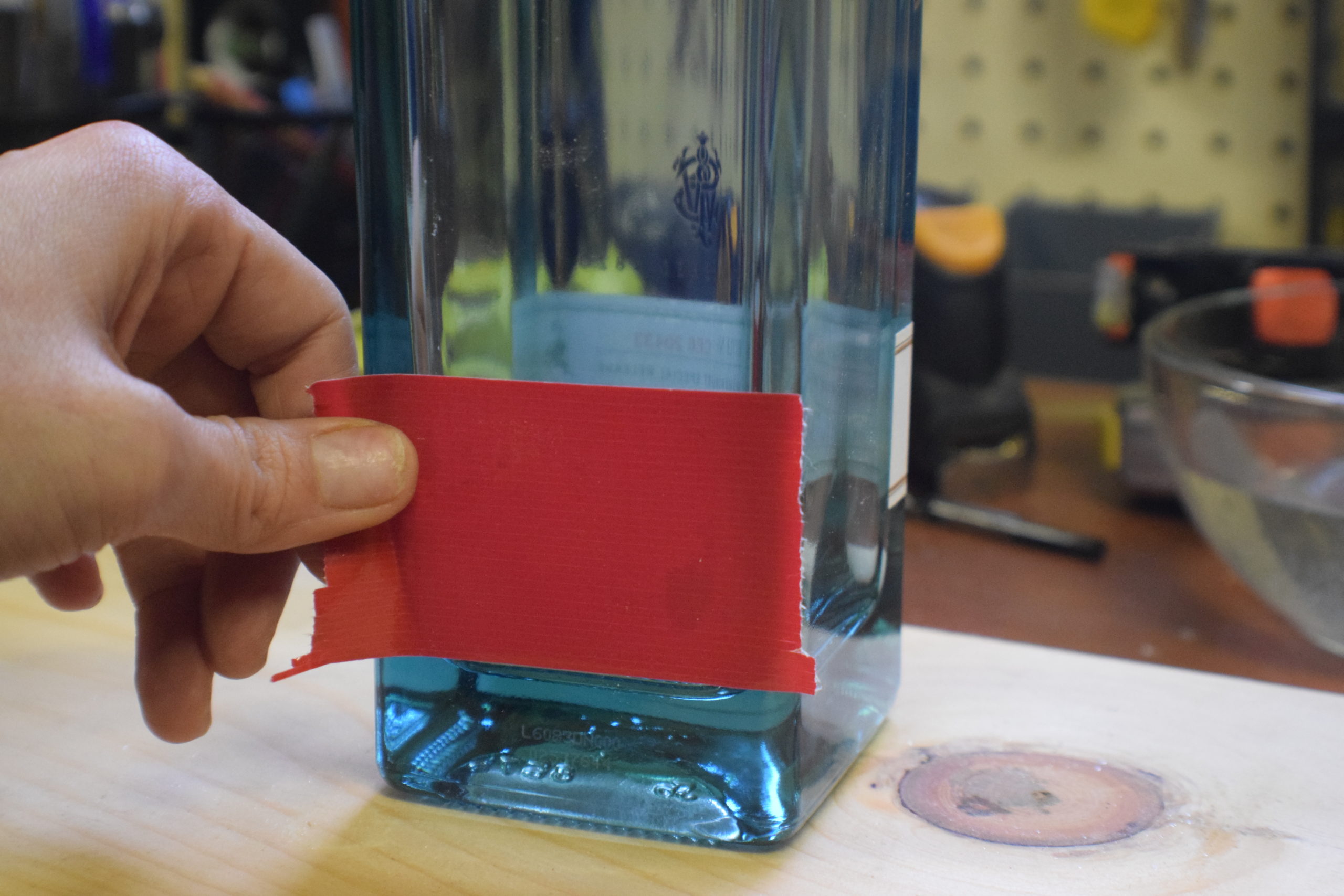 hand putting red duct tape onto square glass bottle in workshop