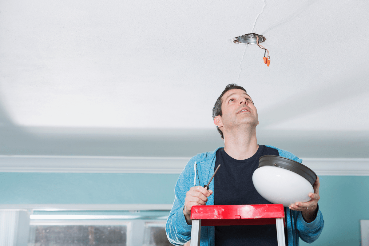 man installing a flush mount light fixture standing on ladder