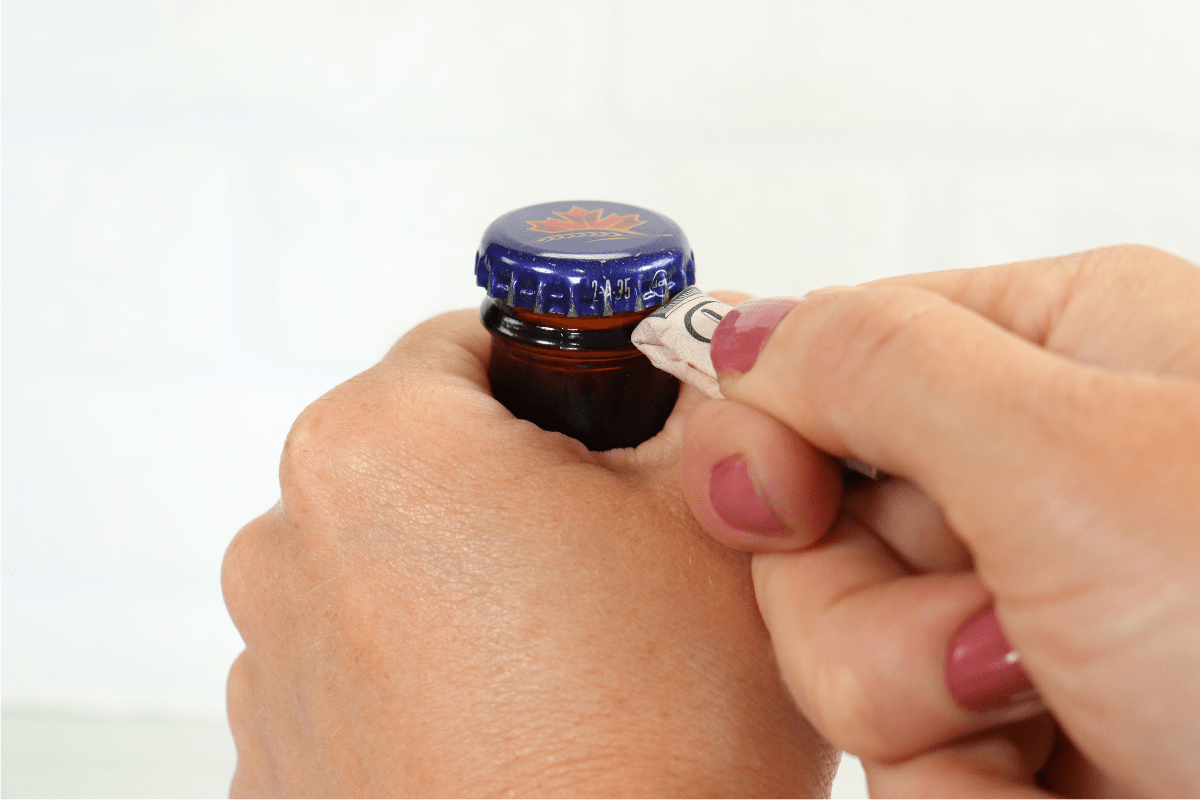 woman hand with pink nail polish using dollar bill to open beer bottle white background