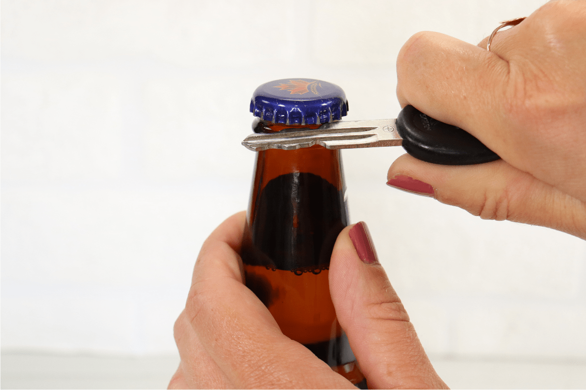 woman hand with pink nail polish using car key to open beer bottle