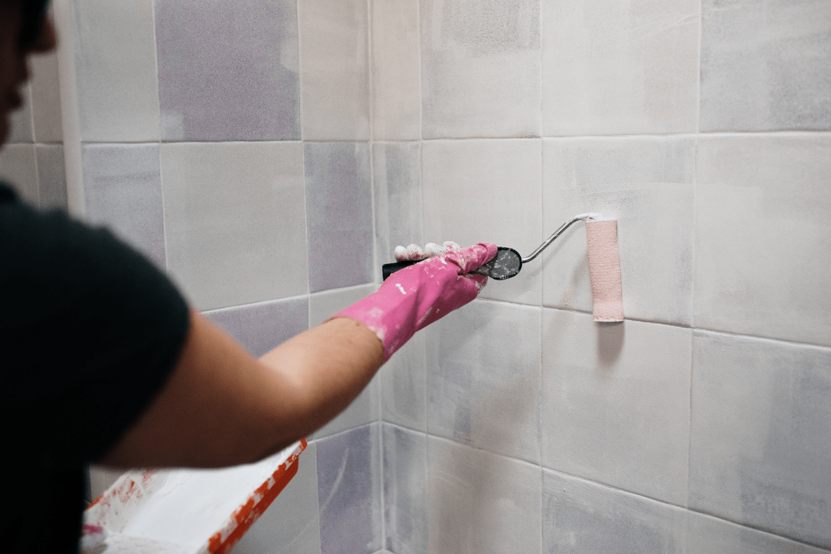 woman painting tile with pink glove and roller