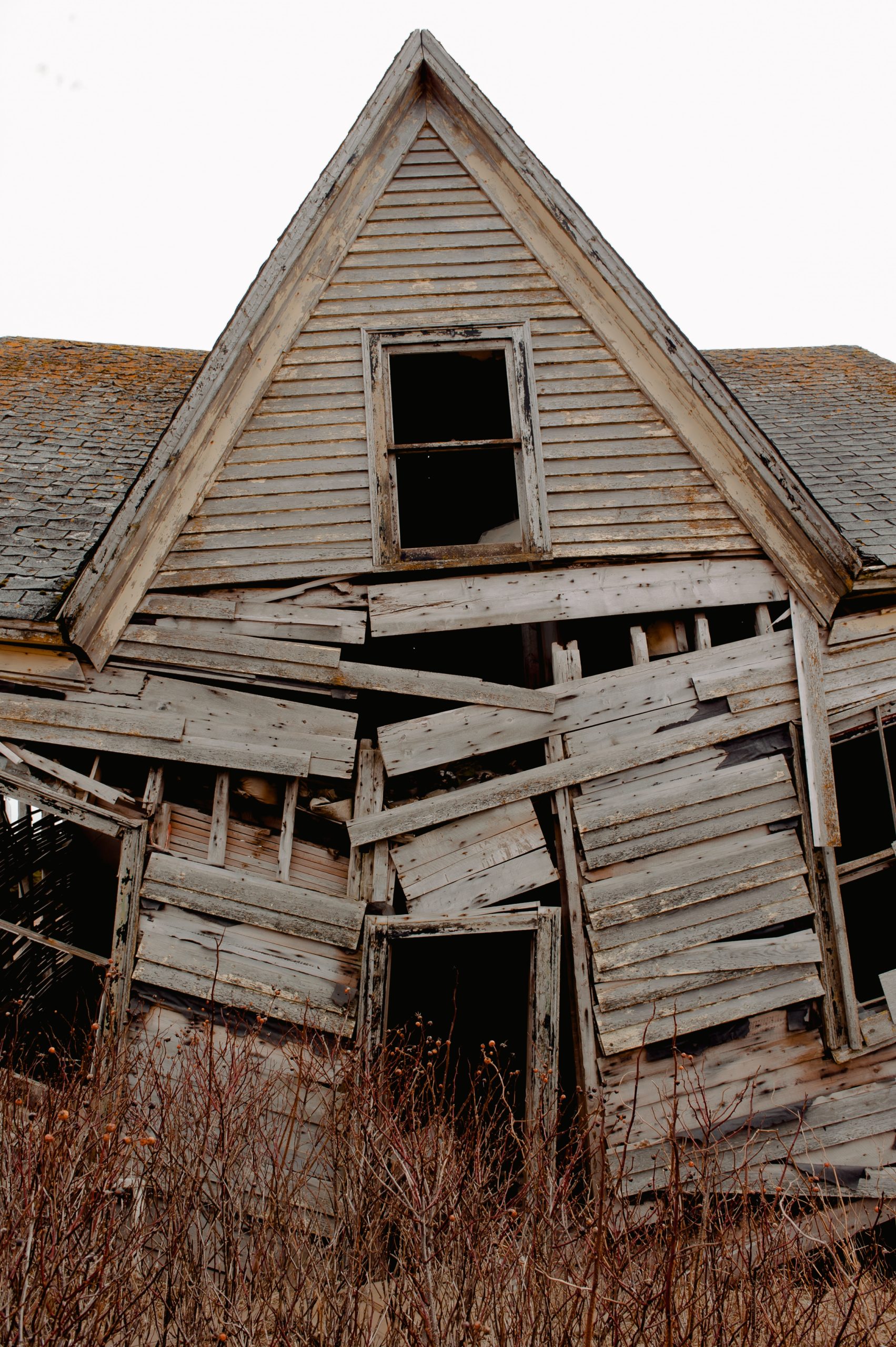 old wooden house falling apart in overgrown area