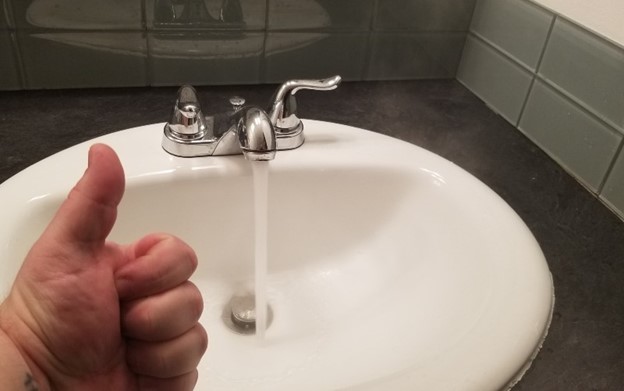 thumbs up in front of a sink with running water