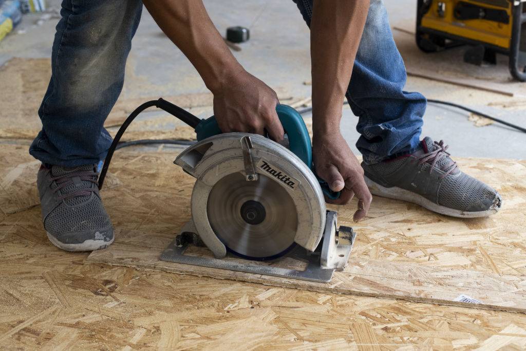 A worker uses a circular saw to cut a piece of flooring