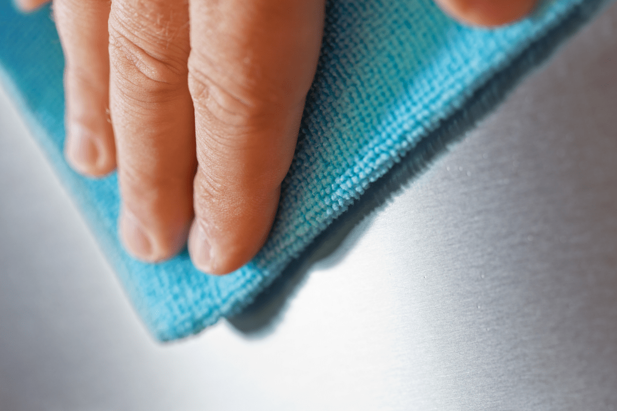 close up of hand rubbing stainless steel with blue microfibre cloth