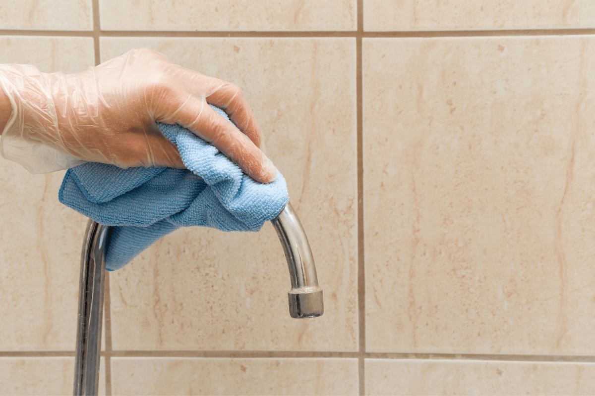 hand wiping chrome faucet with blue mircofibre cloth