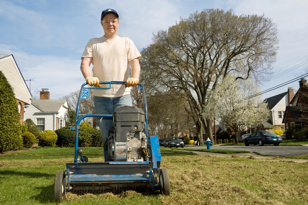 man in white shirt pushing a mechanical power rake across grass