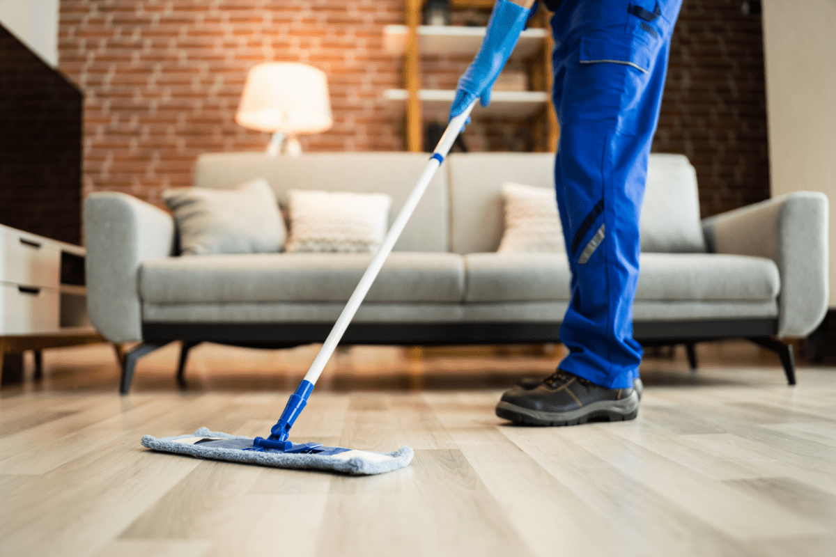 close up of man's legs cleaning vinyl floor with grey couch in the background