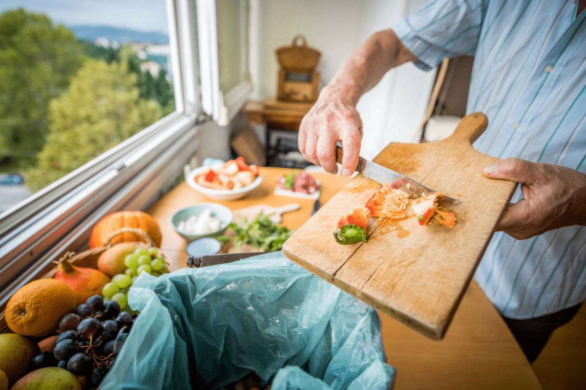 person scraping cutting board food scraps into compost bin on kitchen counter