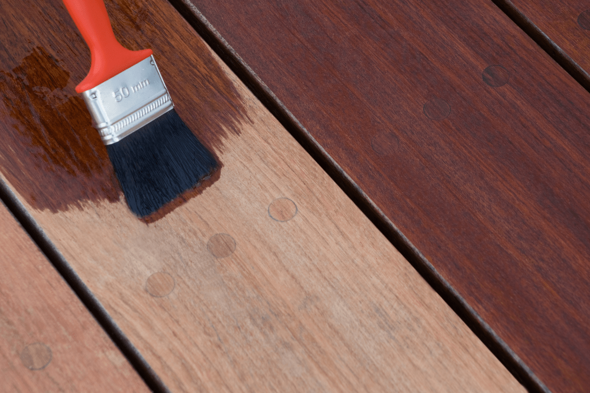 close up of red paint brush being used to stain wood deck