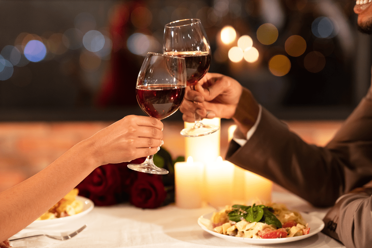 two people having candlelit dinner, cheersing glasses of red wine