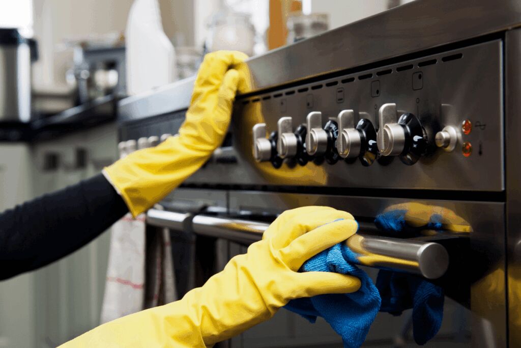 close up on exterior of gas oven with person wearing rubber gloves cleaning it