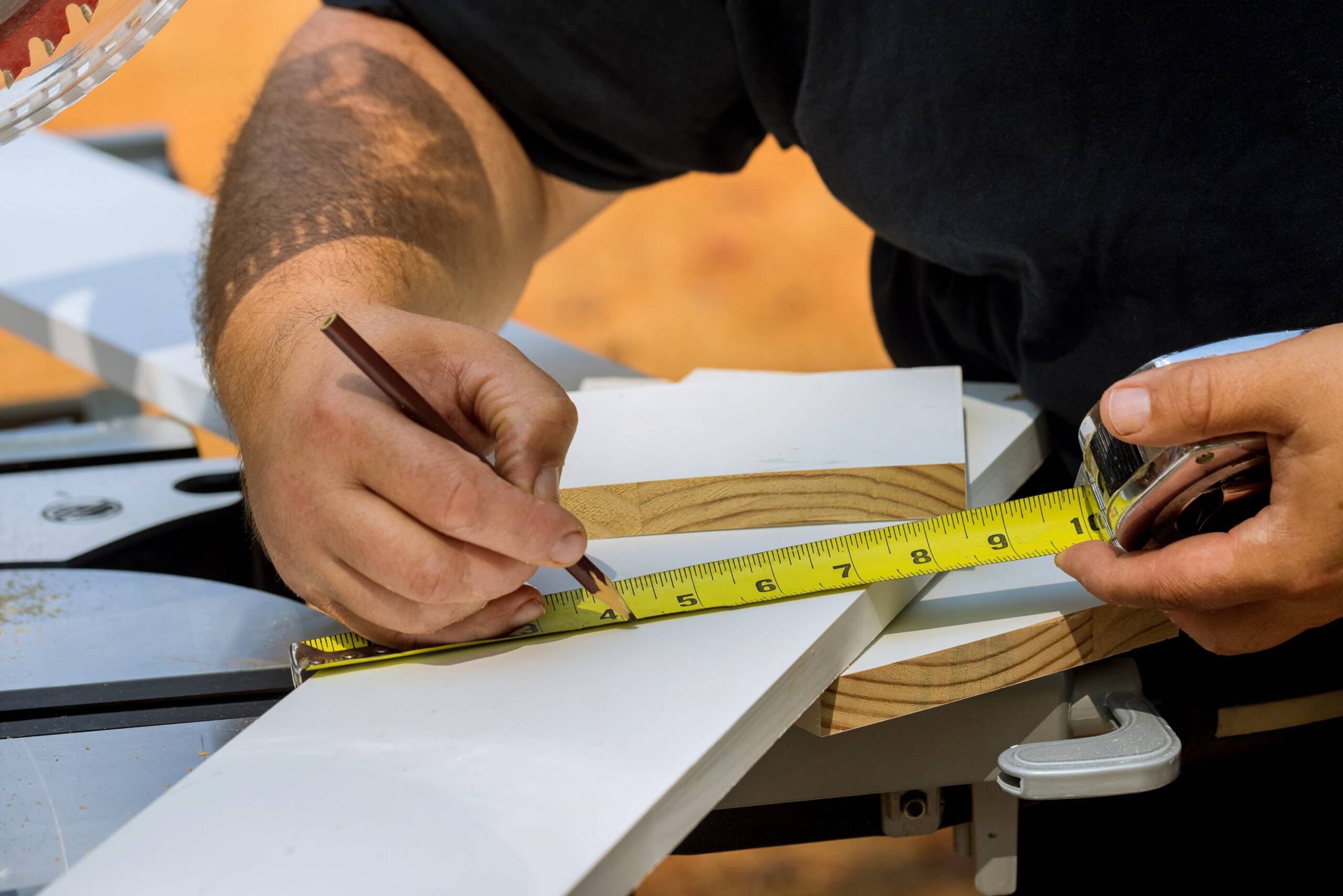 Woodworker preparation for sawing in man measures a piece of wood with tape measure.