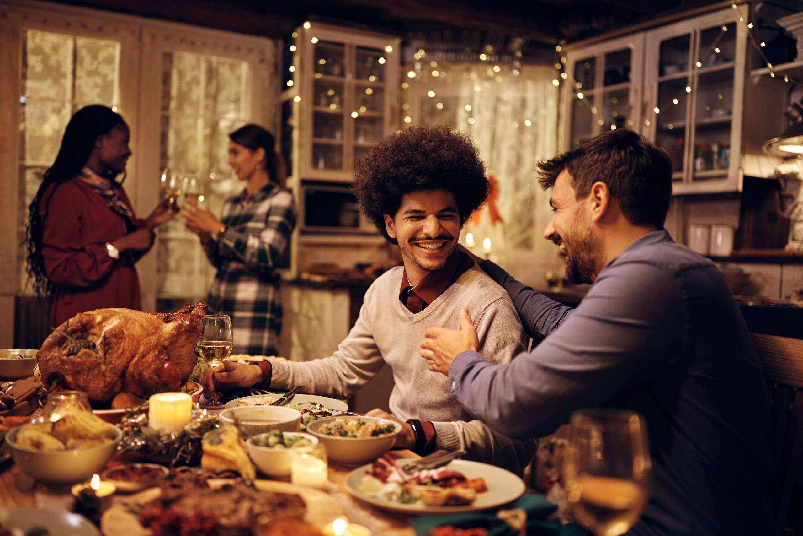 Cheerful male friends having fun while communicating in dining room on Thanksgiving.