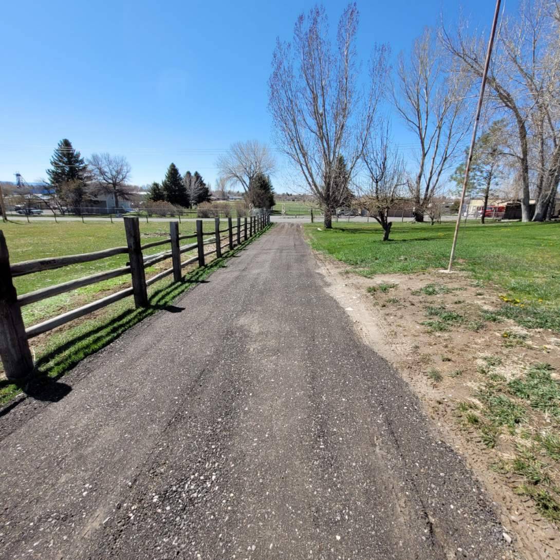 A laneway made of crushed asphalt parallel to a wooden fence.