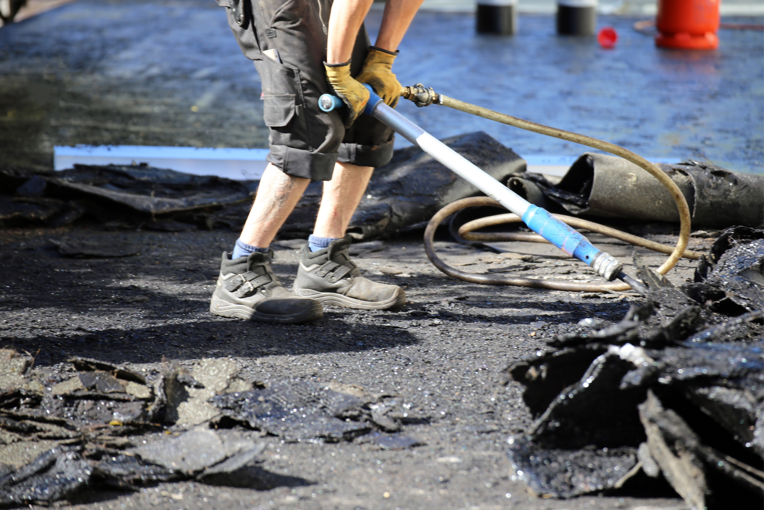 Roofer using heavy-duty tool to remove roof weatherproof material.