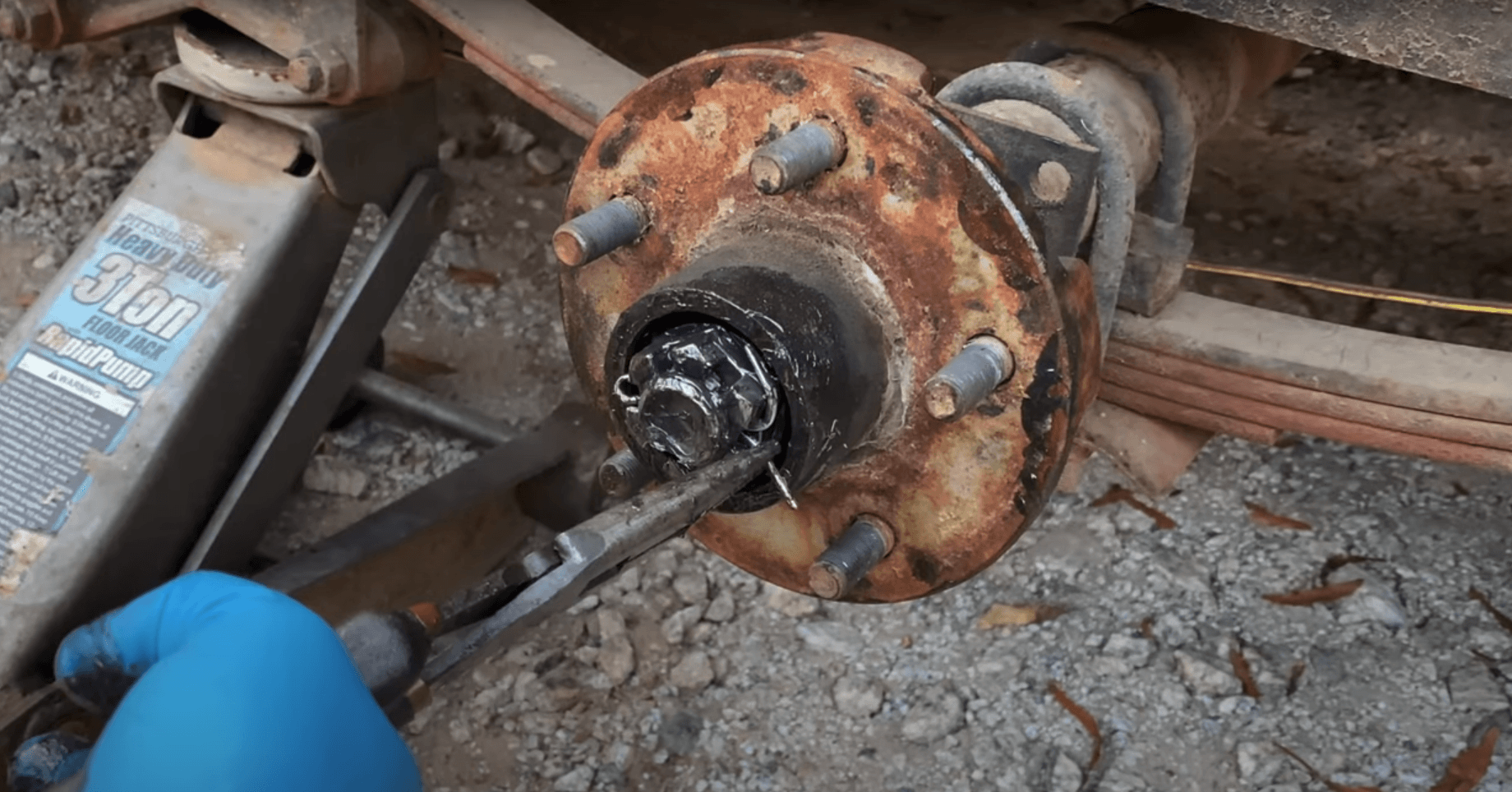 Closeup of rusty trailer hub with wheel removed, showing a greasy crown nut and cotter pin.