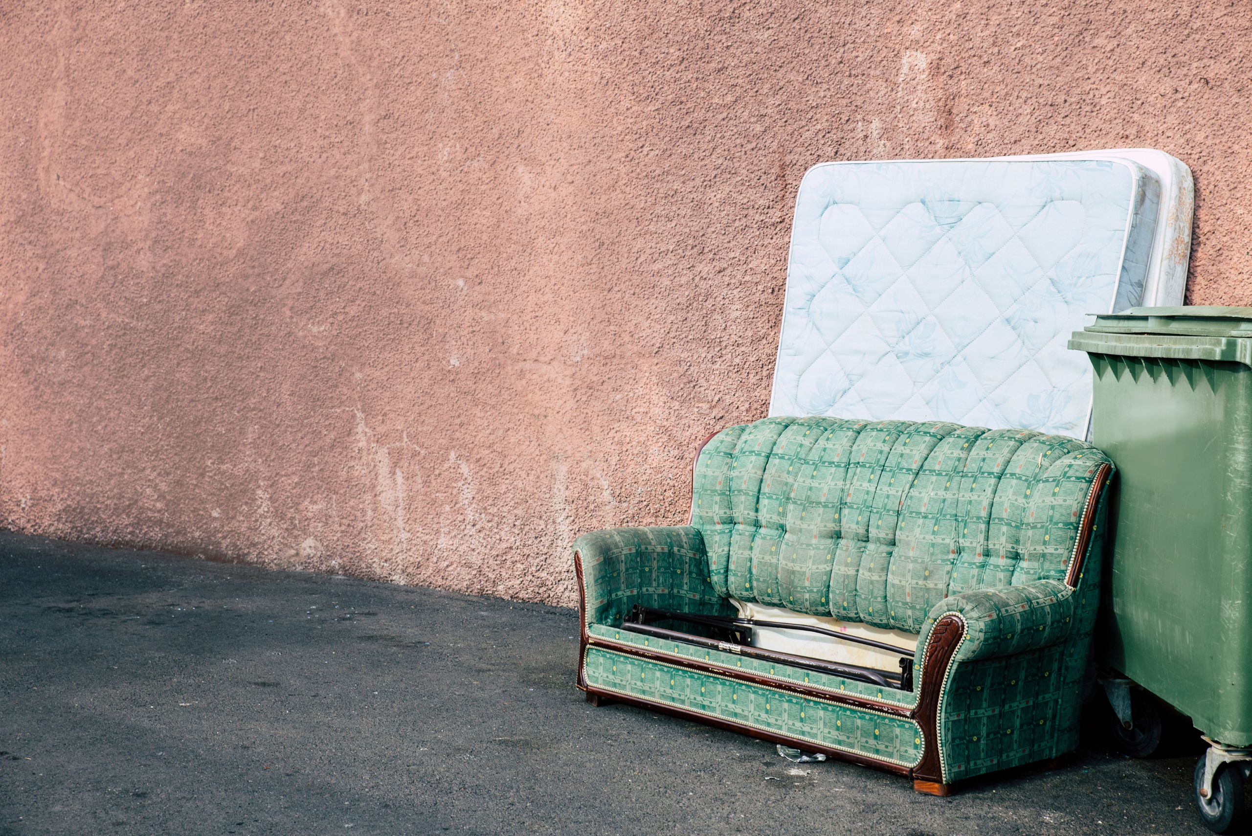 Couch and two mattresses near a dumpster.