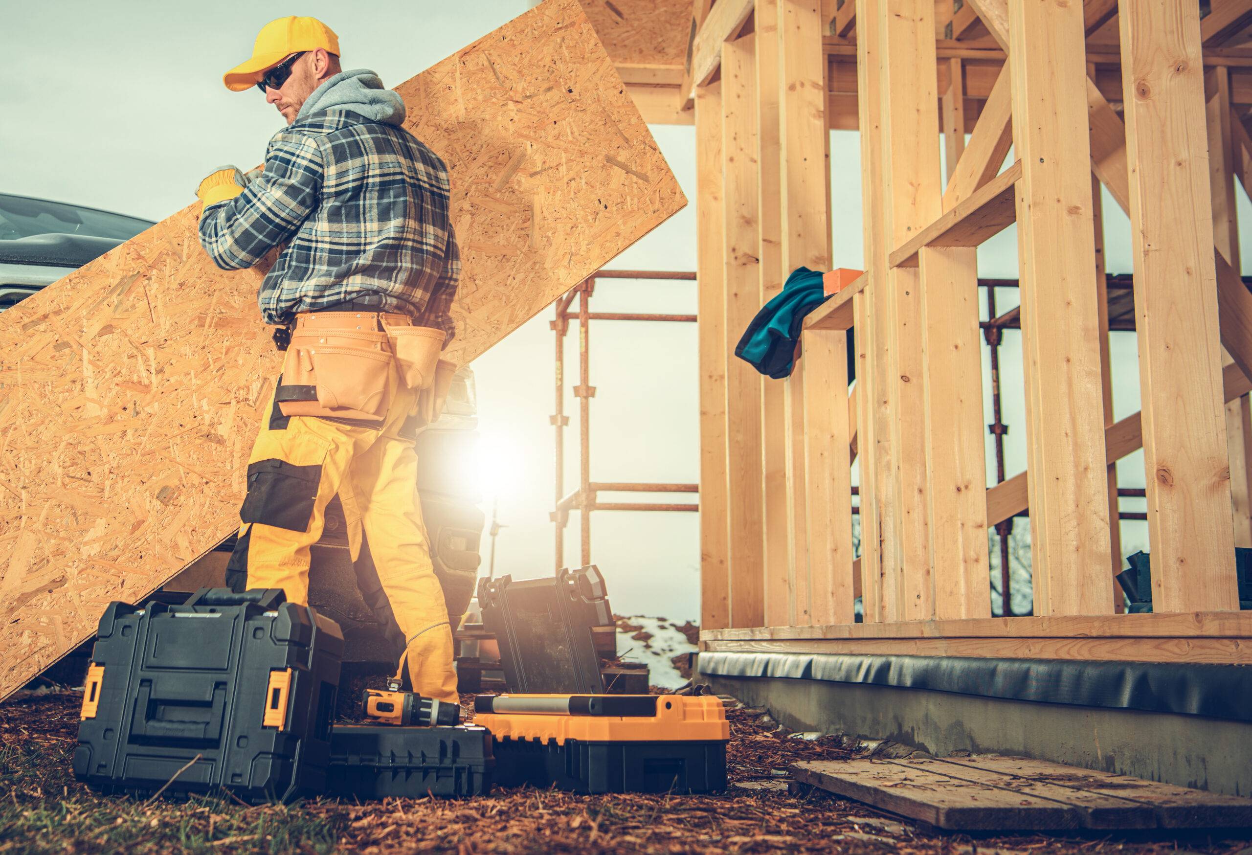 Construction worker carrying plywood sheet.