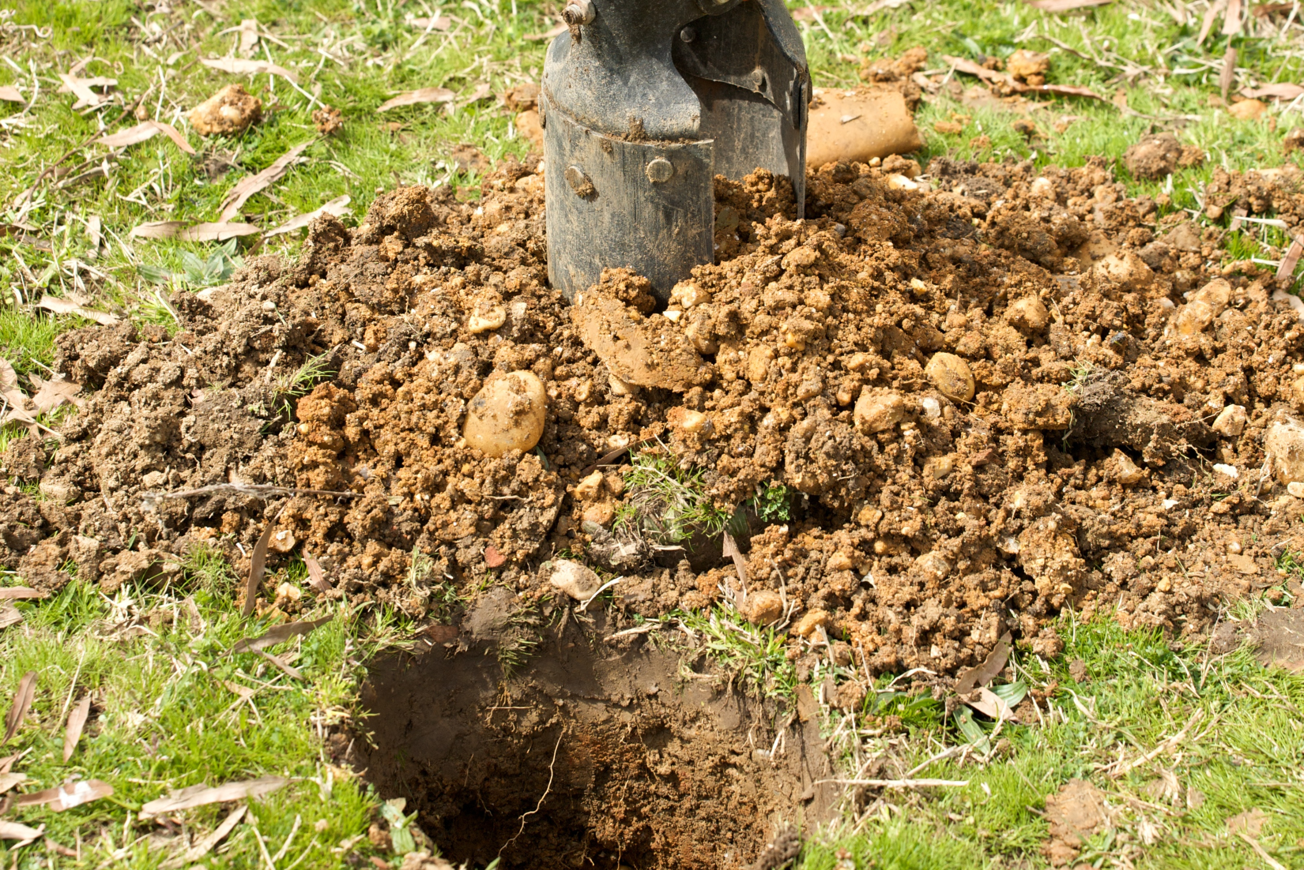 Removing dirt from the hole using a manual post hole digger.