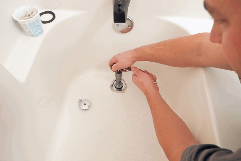 Person using special tool to tighten bathtub drain back on with paste.
