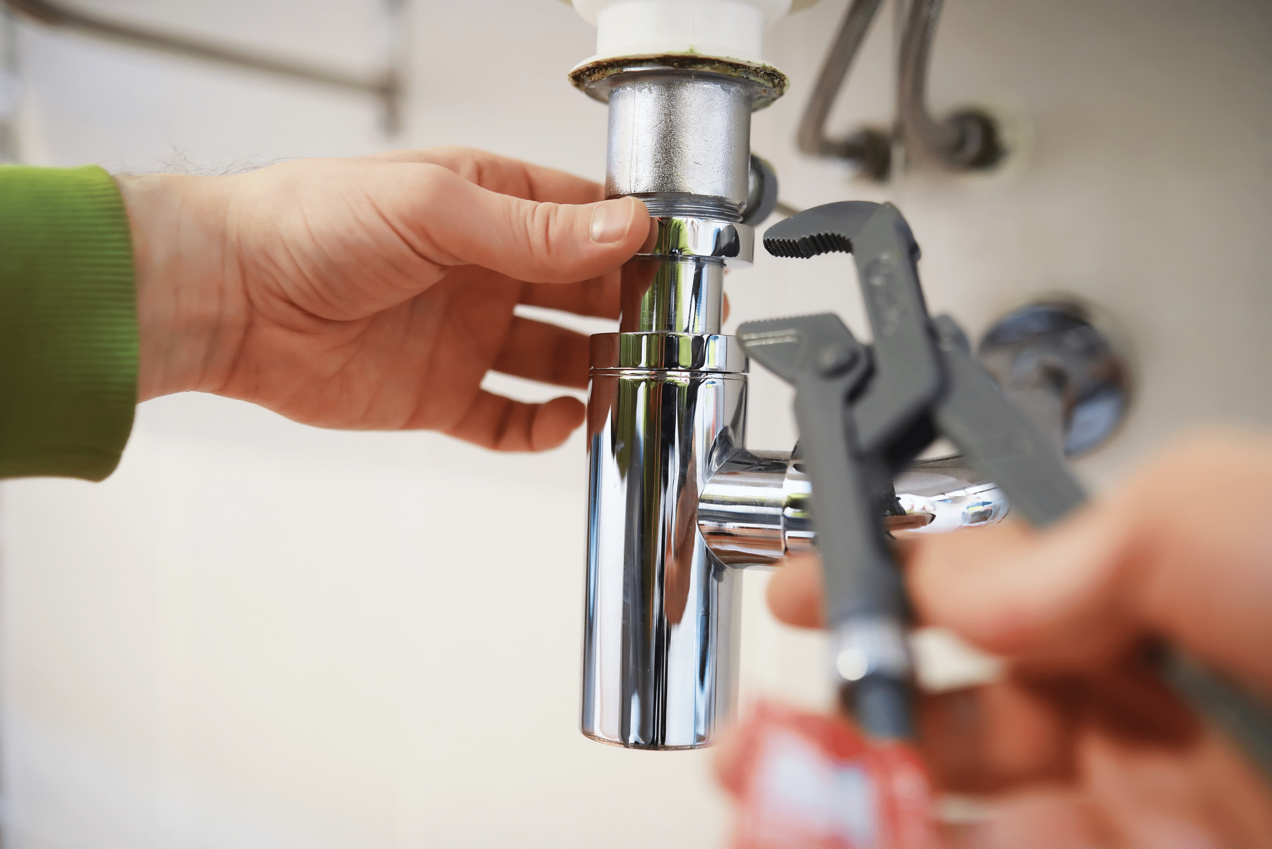 Closeup of monkey wrench and hand by a sink drain tube.